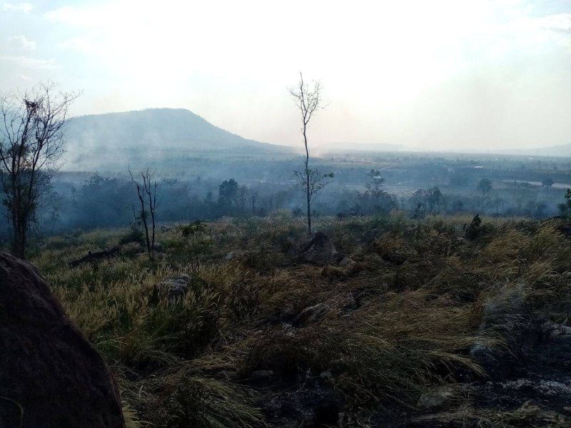 A flat-topped hill seen through smoke, above burnt grassland