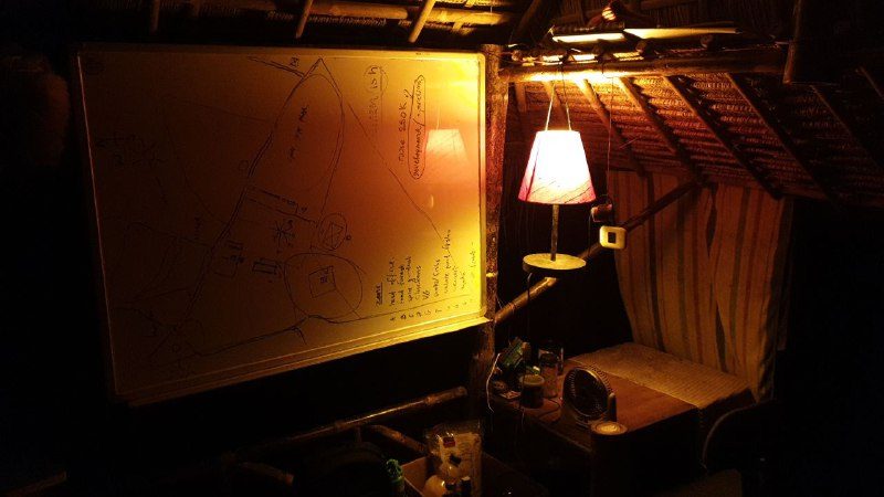 The inside of the hut at night, lit by a lamp, with a whiteboard covered in notes