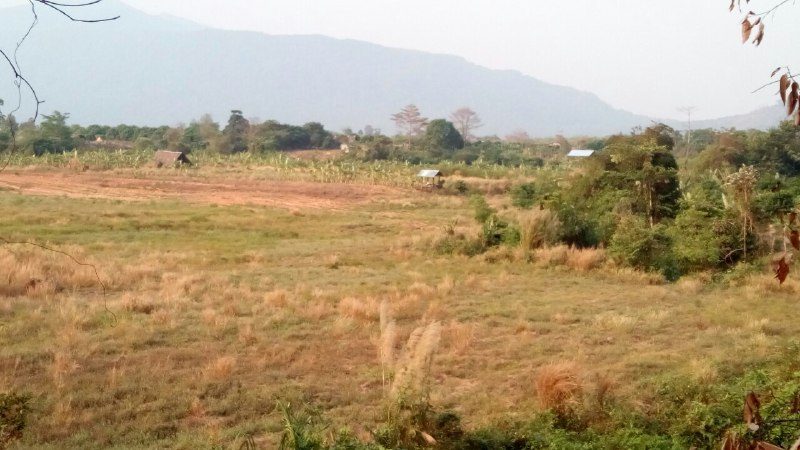 Dry fields with a few huts and trees, and mountains in the haze behind