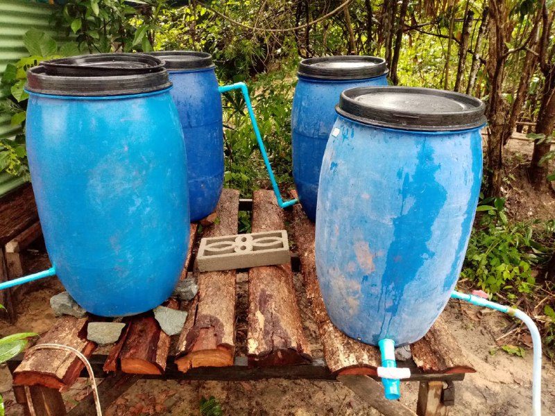 Four blue plastic barrels on a wooden stand, connected by pipes